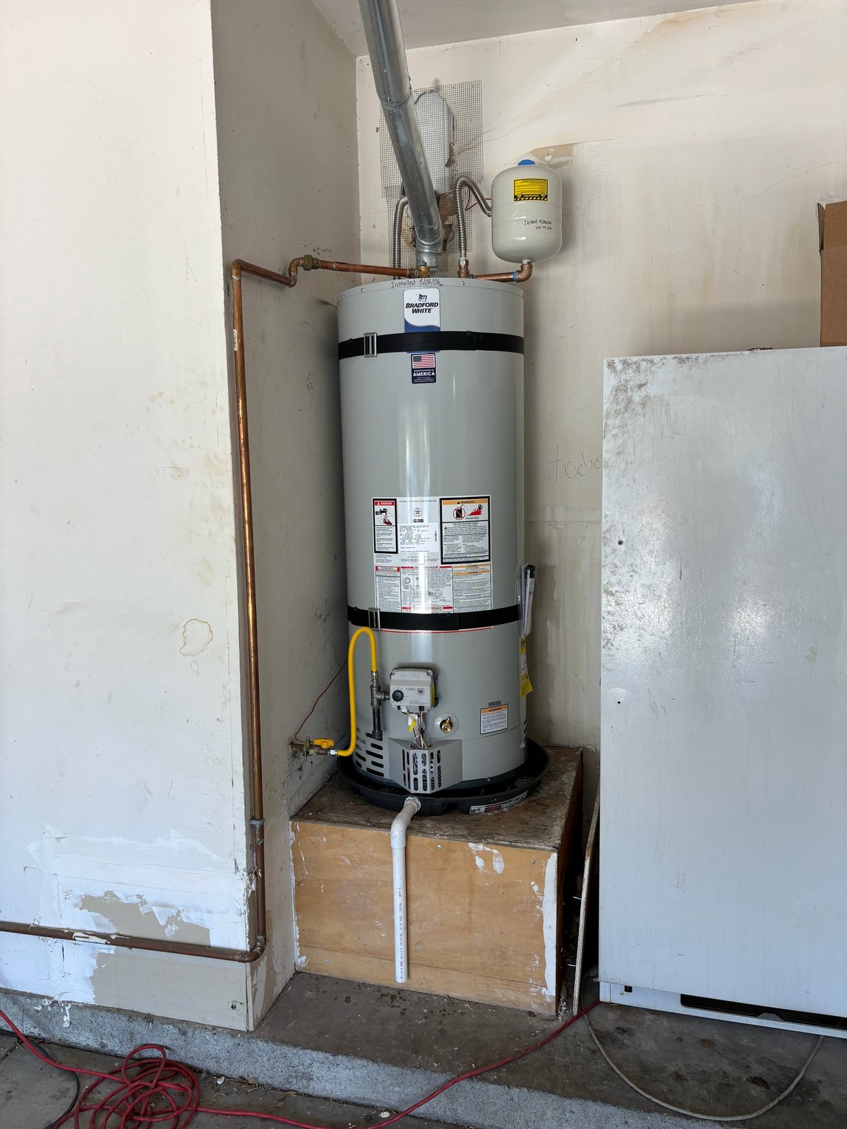 Gas water heater installed in basement corner with copper piping connections and cardboard insulation base