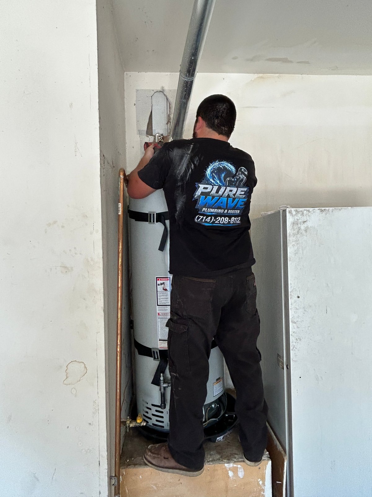 Plumber in Pure Wave shirt working on water heater installation in narrow utility space